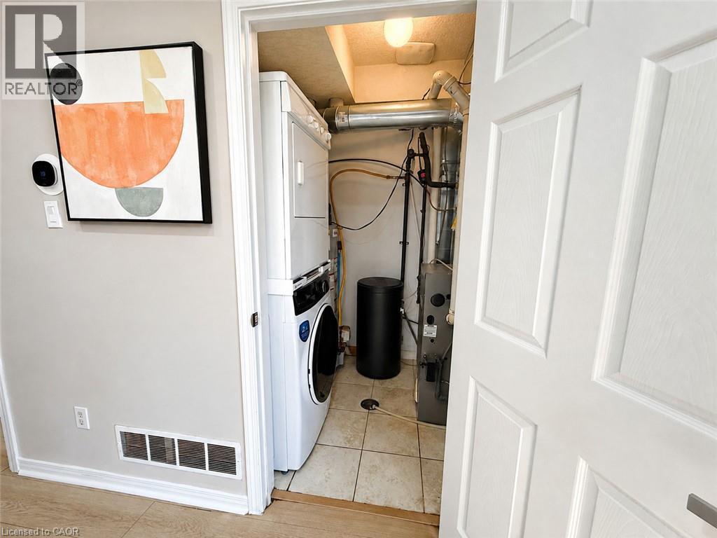 Enclosed utility area featuring a stacked washer and dryer, tile flooring, and a white paneled door - 67 Kinzie Avenue, Kitchener, ON - Indoor Photo Showing Other Room