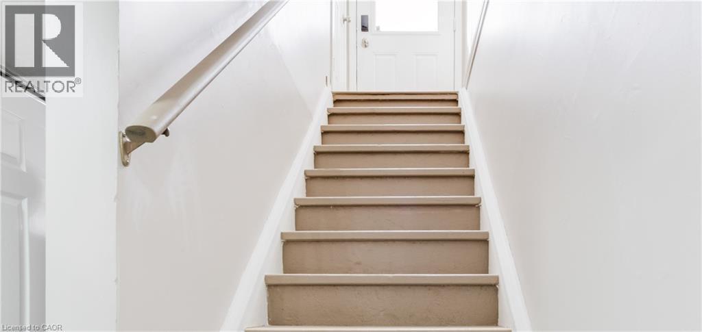 Staircase featuring carpeted treads, a wall-mounted handrail, and a paneled door - 67 Kinzie Avenue, Kitchener, ON - Indoor Photo Showing Other Room