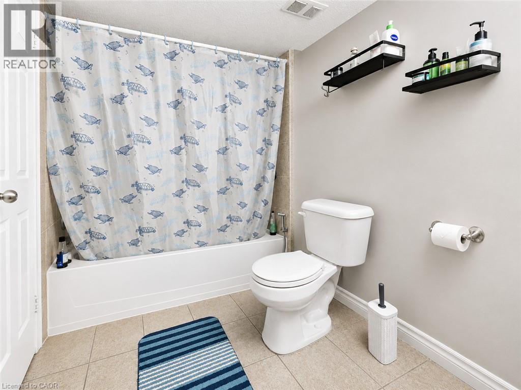 Integrated bathtub with shower, neutral wall tile, white toilet, and neutral tile flooring - 67 Kinzie Avenue, Kitchener, ON - Indoor Photo Showing Bathroom