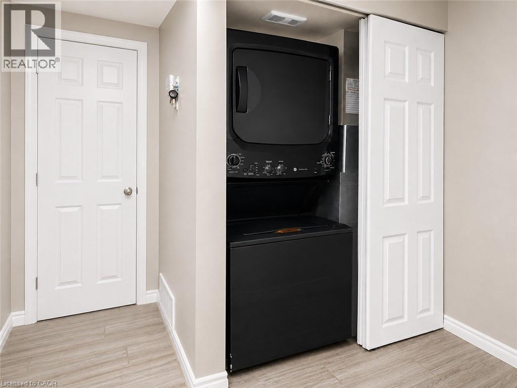 Built-in stackable laundry unit with wood-finish flooring and light-toned wall paint - 67 Kinzie Avenue, Kitchener, ON - Indoor
