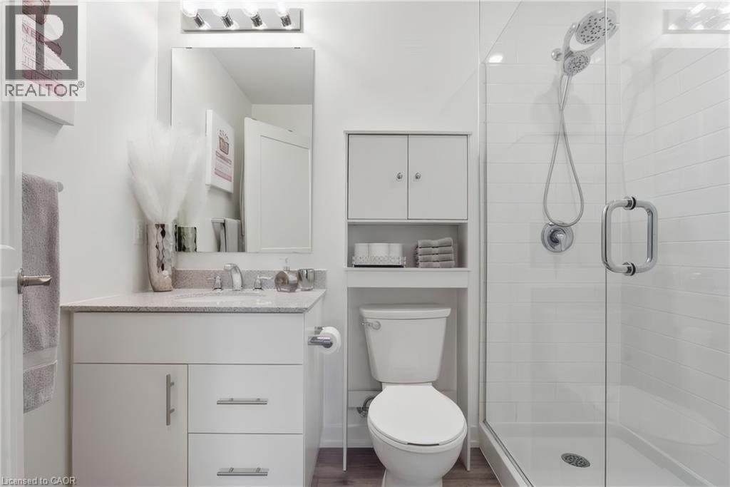 White vanity with a light-toned countertop, rectangular mirror, glass-enclosed shower, and built-in shelving - 251 Northfield Drive E Unit# 312, Waterloo, ON