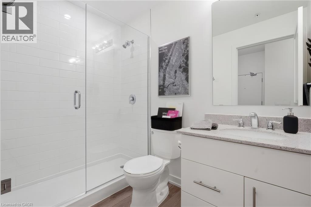 Glass-enclosed shower with white subway tile, single vanity with light-colored countertop, integrated sink, and wood-finish flooring - 251 Northfield Drive E Unit# 312, Waterloo, ON