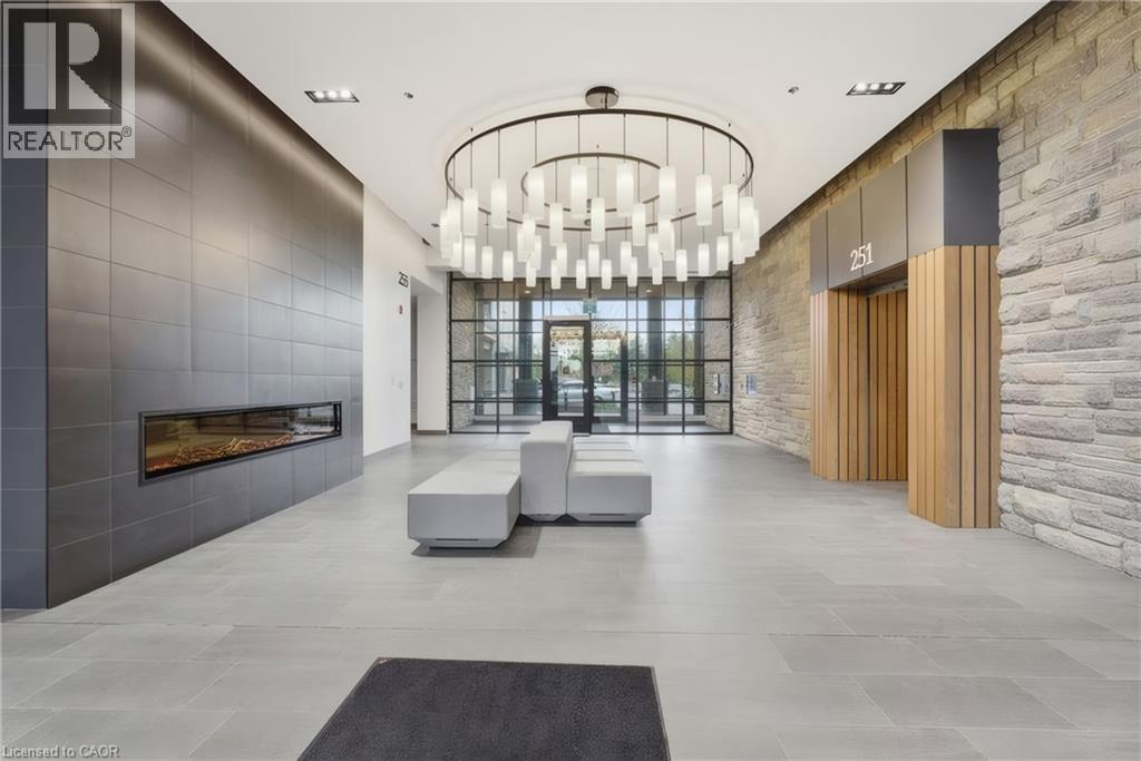Spacious lobby featuring a linear electric fireplace, large format tile flooring, stone accent wall, and a round chandelier with multiple lights - 251 Northfield Drive E Unit# 312, Waterloo, ON