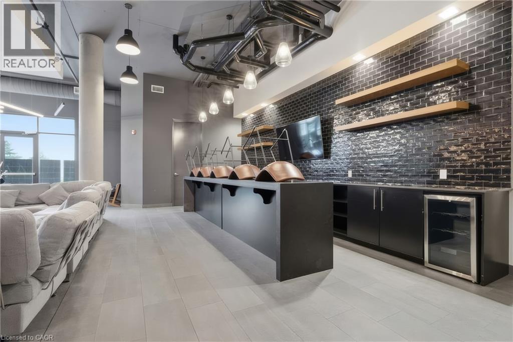 Modern amenity area featuring large format tile flooring, black subway tile accent wall, built-in cabinetry, integrated beverage cooler, and large windows providing natural light - 251 Northfield Drive E Unit# 312, Waterloo, ON