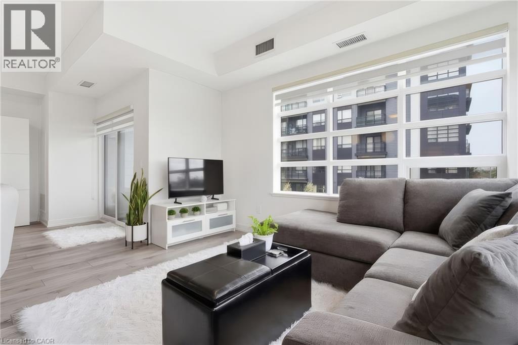 Spacious living area featuring expansive windows, wood-finish flooring, and white walls - 251 Northfield Drive E Unit# 312, Waterloo, ON