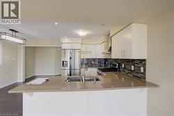 Kitchen featuring a breakfast bar with stone-finish countertop, stainless steel appliances, white cabinetry, and mosaic tile backsplash - 