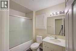 Bathroom featuring a built-in bathtub with sliding frosted glass enclosure, white wall tiling, a vanity with an integrated sink, and a wall-mounted mirror - 