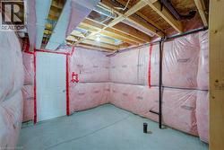 Unfinished basement space featuring exposed wood joists, insulated walls, concrete flooring, and a panel door - 