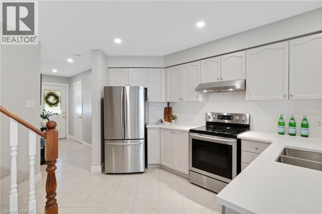 Bright kitchen featuring white cabinetry, stainless steel appliances, a white tile backsplash, light countertops, and recessed lighting - 711 Angler Way, Waterloo, ON - Indoor Photo Showing Kitchen With Double Sink