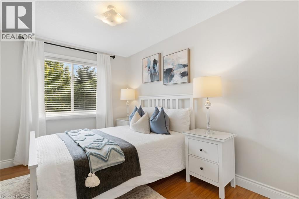 Light-colored walls with wood-finish flooring, featuring a window with white blinds and curtains, and a ceiling-mounted light fixture - 711 Angler Way, Waterloo, ON - Indoor Photo Showing Bedroom