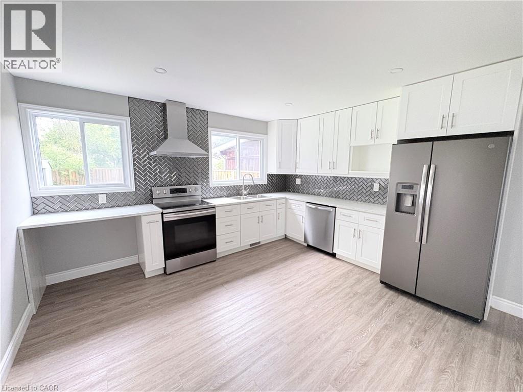 Updated kitchen featuring white shaker cabinetry, stainless steel appliances, herringbone tile backsplash, and wood-finish flooring - 216 Brunswick Crescent, London, ON