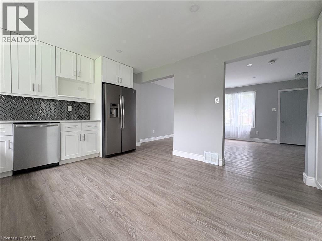 Modern kitchen with white cabinetry, stainless steel appliances, herringbone tile backsplash, and wood-finish flooring - 216 Brunswick Crescent, London, ON