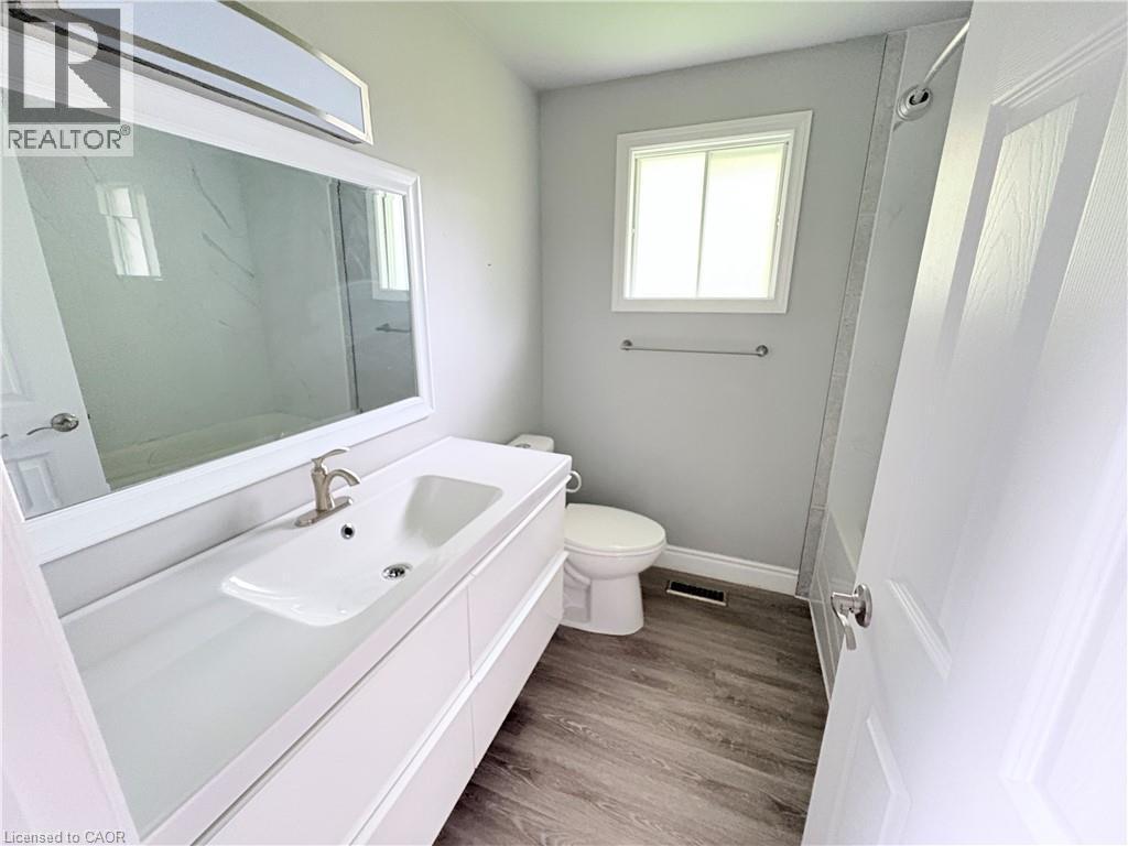 Bathroom featuring wood-finish flooring, a white vanity with an integrated sink, a rectangular framed mirror, and a window - 216 Brunswick Crescent, London, ON