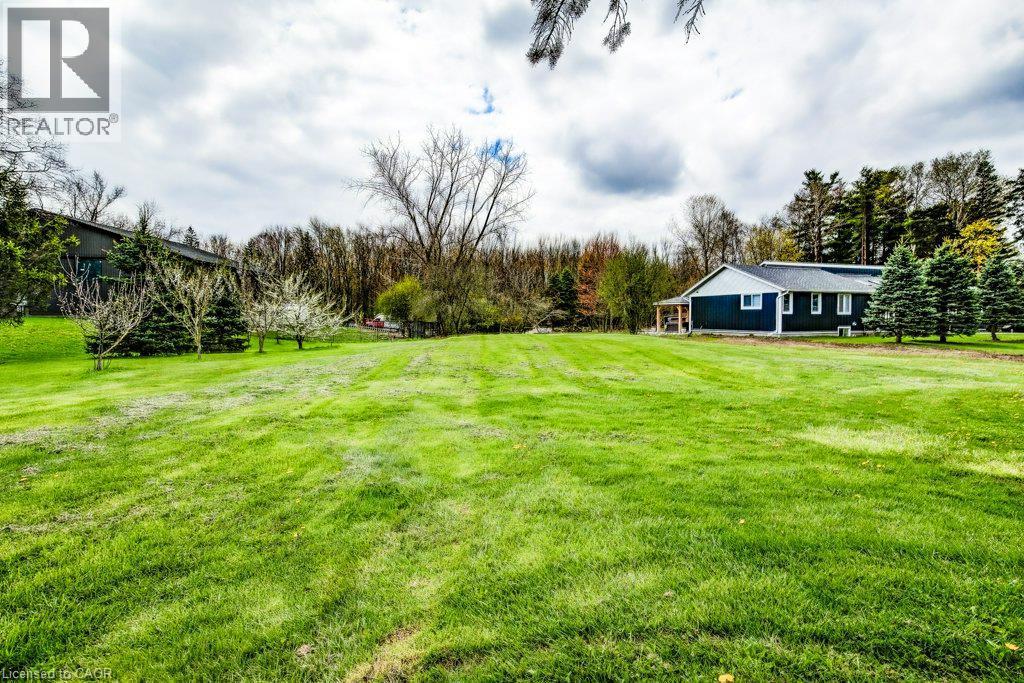 Expansive green lawn with a home featuring dark blue siding and a covered porch - 121 Dodge Drive, Kitchener, ON
