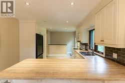 Kitchen featuring a large breakfast bar with a stone-finish countertop, white cabinetry with crown molding, recessed lighting, a stainless steel sink with a gooseneck faucet, and a dark subway tile ba - 