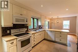 Kitchen featuring extensive cream cabinetry, a built-in microwave, a black subway tile backsplash, recessed lighting, and a kitchen island with pendant lighting - 