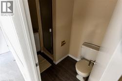 Bathroom featuring wood-finish flooring, a white toilet with a brushed metal flush lever, and a shower enclosure with a dark-framed glass door - 