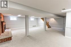 Spacious finished basement featuring light-toned carpeting, a brick fireplace with a stone hearth, recessed lighting, and paneling along the walls - 