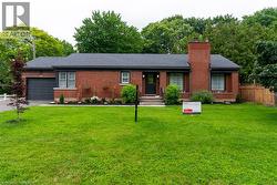 Brick bungalow with a dark gray shingled roof, a prominent brick chimney, and a landscaped front garden - 