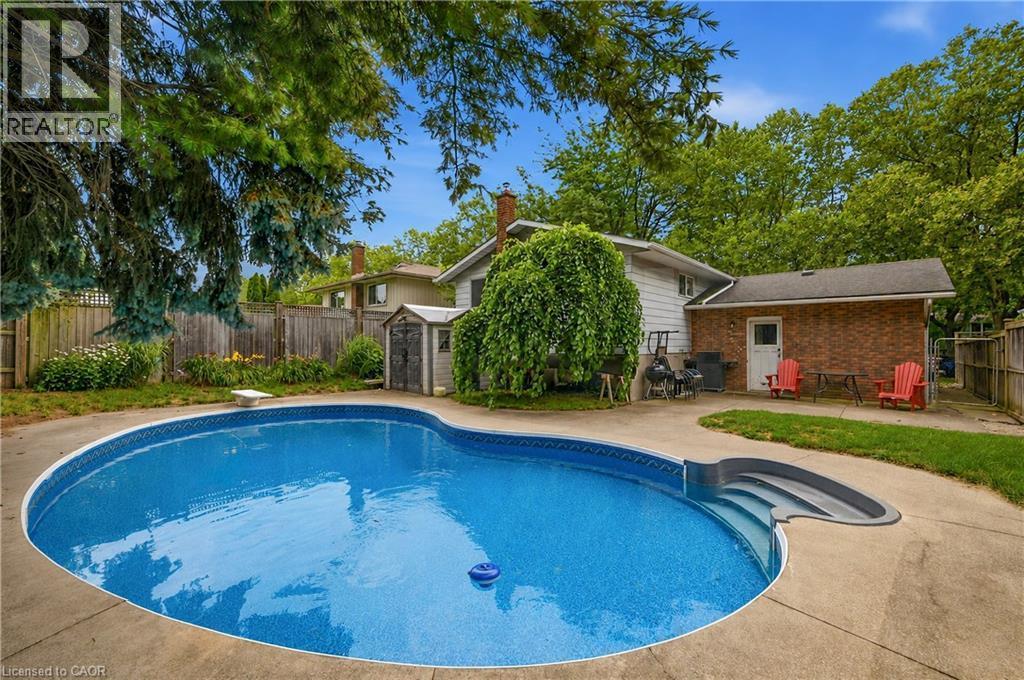 Fenced backyard featuring a kidney-shaped in-ground swimming pool with integrated steps, concrete patio surround, and a storage shed - 11 Kimbermount Drive, St. Catharines, ON - Outdoor With In Ground Pool With Backyard