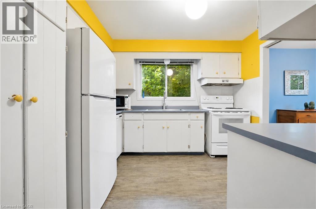 Kitchen featuring wood-finish flooring, white cabinetry with yellow knobs, a white refrigerator, and a white oven with an overhead range hood - 11 Kimbermount Drive, St. Catharines, ON - Indoor Photo Showing Kitchen With Double Sink
