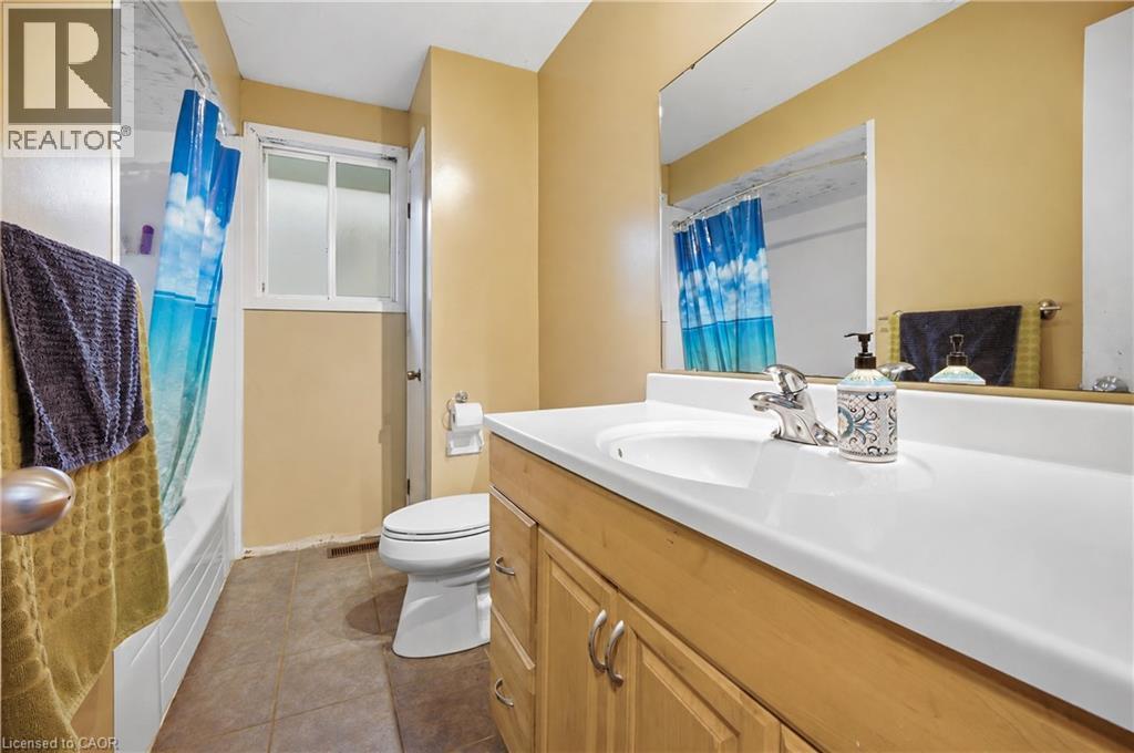 Bathroom featuring a single vanity with a white countertop and light wood-finish cabinetry, a mirror, a toilet, a tub, and a window - 11 Kimbermount Drive, St. Catharines, ON - Indoor Photo Showing Bathroom