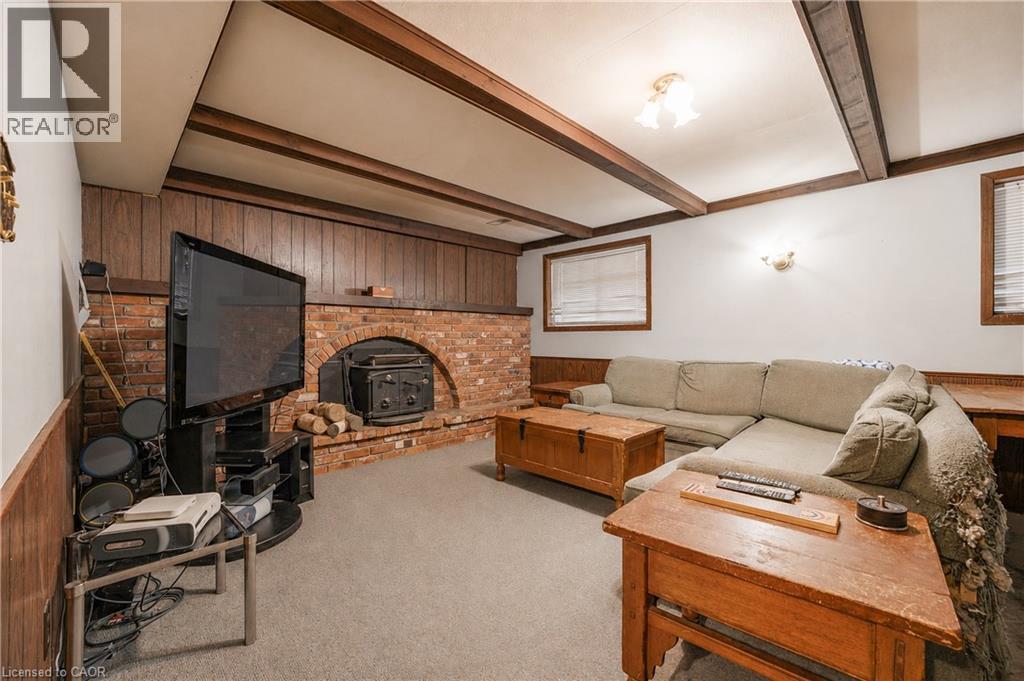 Spacious living area featuring a brick fireplace surround, wood paneling, and exposed ceiling beams - 11 Kimbermount Drive, St. Catharines, ON - Indoor Photo Showing Living Room With Fireplace