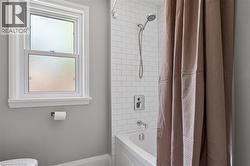 Bathtub with subway tile surround, polished chrome fixtures, and a double-hung window with privacy glazing -