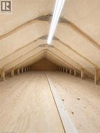 Attic space featuring spray foam insulation, exposed wood rafters, plywood flooring, and a fluorescent light fixture -