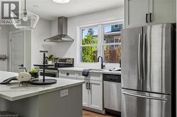 Kitchen featuring stainless steel appliances, white cabinetry, a kitchen island with stone-finish countertop, and a contemporary pendant light fixture -