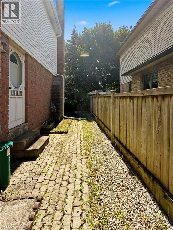 Paver stone pathway leading to a treed area, bordered by a wood fence and gravel landscaping - 512 Hawthorne Crescent, Milton, ON - Outdoor With Exterior