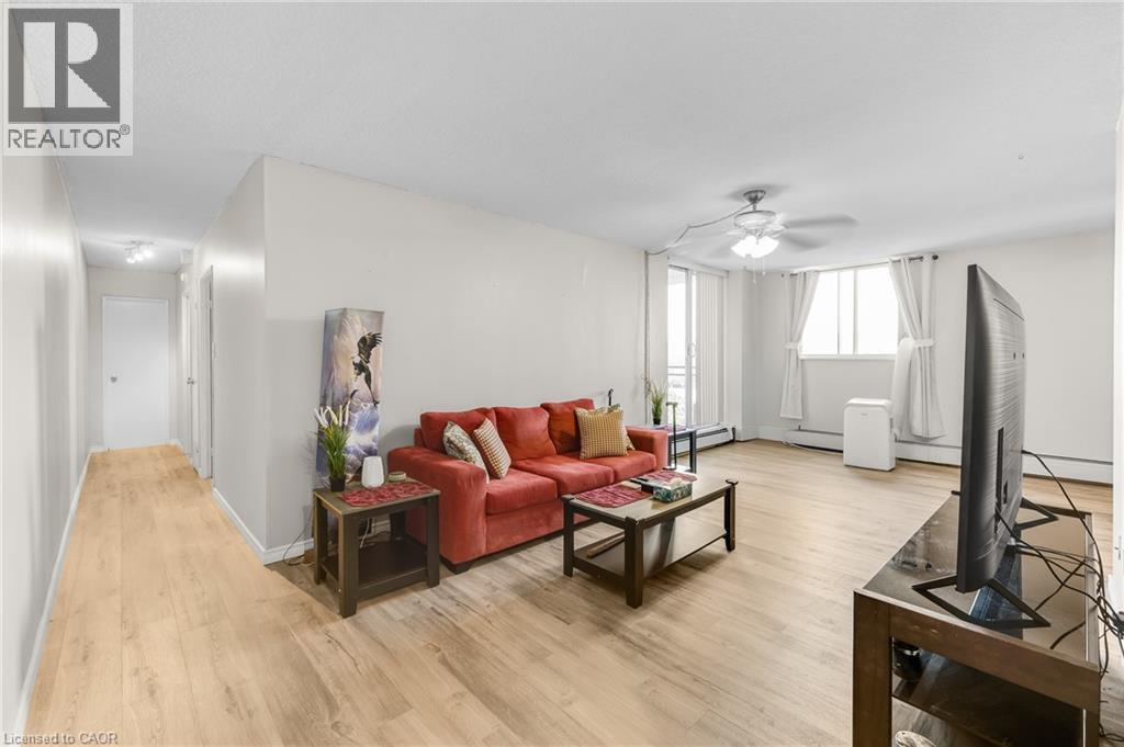 Spacious room with wood-finish flooring, a ceiling fan, and large windows - 975 Warwick Court Unit# 708, Burlington, ON - Indoor Photo Showing Living Room