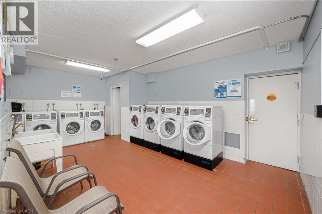 Laundry facility featuring multiple front-loading washers, utility sink, terra cotta-style flooring, and fluorescent lighting - 975 Warwick Court Unit# 708, Burlington, ON - Indoor Photo Showing Laundry Room