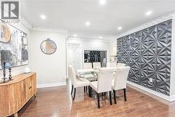Dining area featuring a prominent textured accent wall, rich wood-finish flooring, recessed lighting, crown molding, and substantial baseboards -