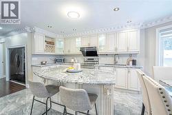 Kitchen featuring an oversized island with a stone countertop, white cabinetry with decorative molding, stainless steel appliances, and large format floor tiles -