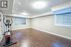 Spacious interior room featuring wood-finish flooring, neutral wall tones, and multiple windows with horizontal blinds -