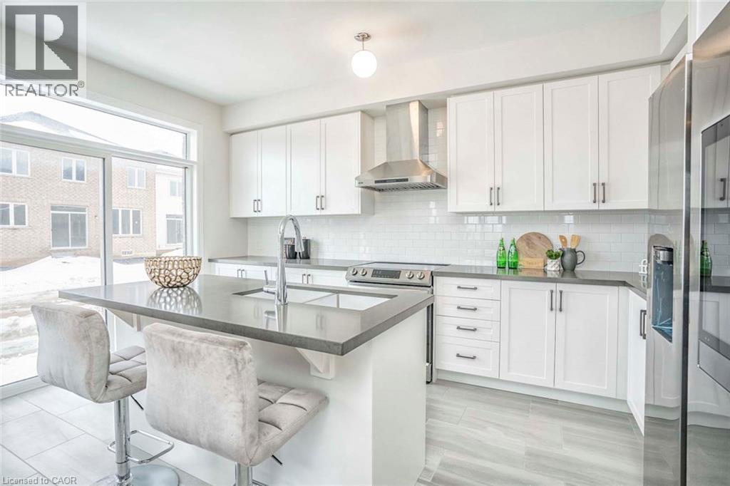 Modern kitchen featuring white cabinetry, subway tile backsplash, stainless steel appliances, a center island with an undermount sink, and wood-finish flooring - 525 Red Elm Road, Shelburne, ON - Indoor Photo Showing Kitchen