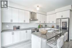 Kitchen featuring white shaker-style cabinetry, grey countertops, subway tile backsplash, and stainless steel appliances -