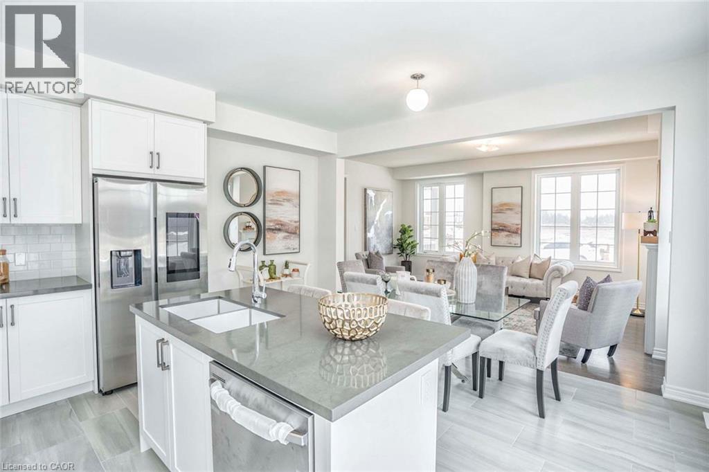 Open concept living space featuring a kitchen island with sink, white shaker cabinetry, stainless steel appliances, and large windows - 525 Red Elm Road, Shelburne, ON - Indoor Photo Showing Kitchen With Upgraded Kitchen