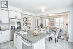 Open concept living space featuring a kitchen island with sink, white shaker cabinetry, stainless steel appliances, and large windows -