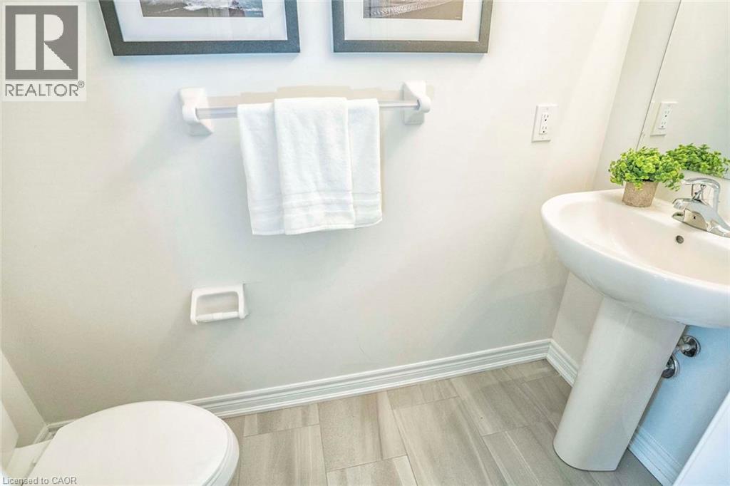 Pedestal sink with chrome faucet, toilet, wall-mounted towel bar, and wood-finish flooring - 525 Red Elm Road, Shelburne, ON - Indoor Photo Showing Bathroom