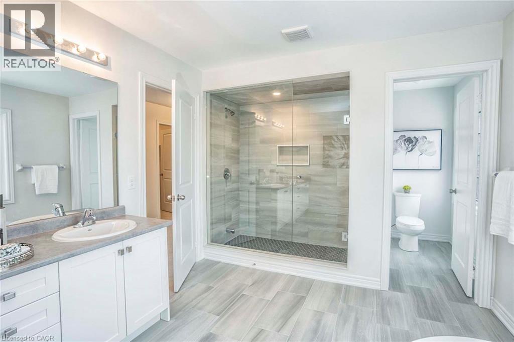 Spa-inspired primary bathroom featuring a frameless glass-enclosed walk-in shower with linear floor drain, dual vanity with white cabinetry and integrated sink, wood-finish plank flooring, and abundan - 525 Red Elm Road, Shelburne, ON - Indoor Photo Showing Bathroom