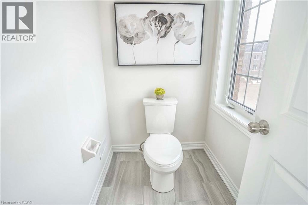 White toilet, wood-finish flooring, white trim, and a window with grid patterns - 525 Red Elm Road, Shelburne, ON - Indoor Photo Showing Bathroom