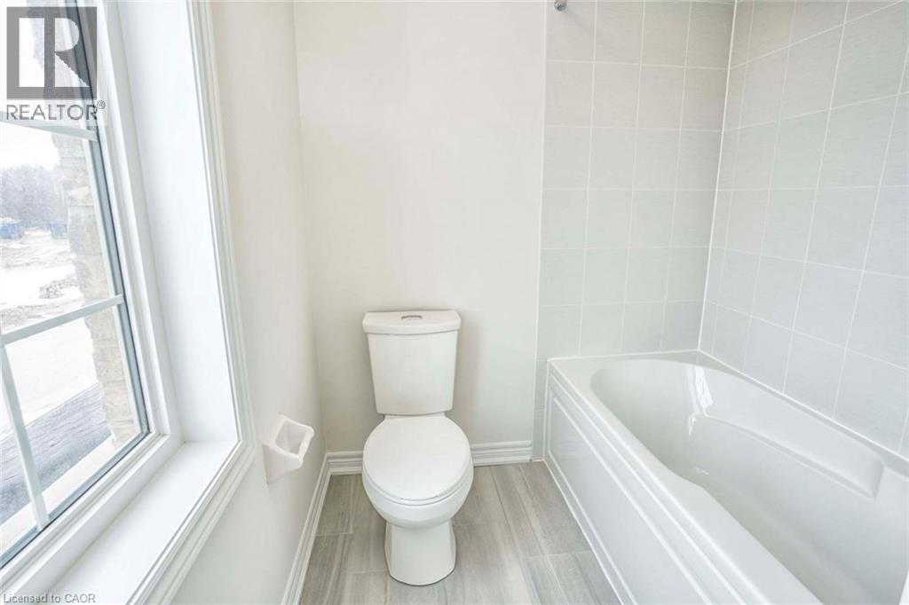 White ceramic tile flooring complementing a standard toilet, a white bathtub, and a window with grid detailing - 525 Red Elm Road, Shelburne, ON - Indoor Photo Showing Bathroom