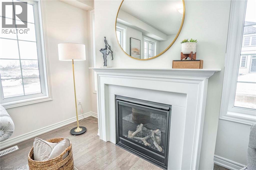 Bright living room anchored by a gas fireplace with surround molding and black metal frame insert, topped with a round brass-framed mirror and wooden mantel shelf - 525 Red Elm Road, Shelburne, ON - Indoor Photo Showing Living Room With Fireplace