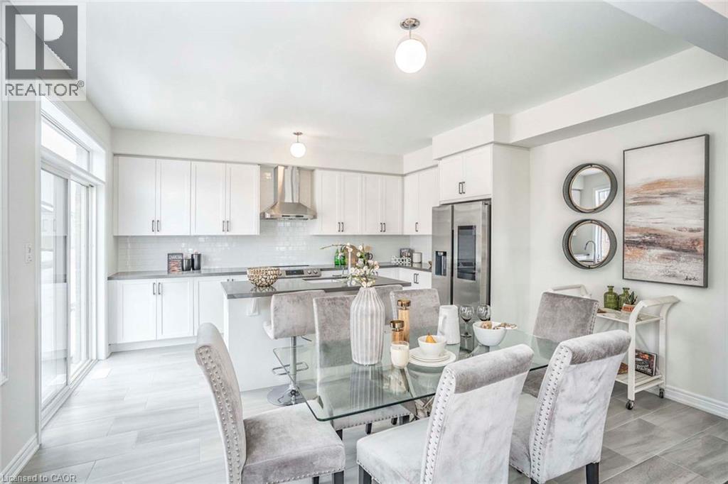 Modern kitchen featuring white cabinetry, stainless steel appliances, a center island with bar seating, and light-toned flooring - 525 Red Elm Road, Shelburne, ON - Indoor