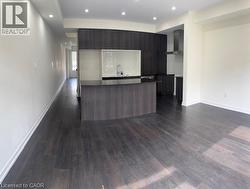 Open-concept kitchen featuring dark wood-finish cabinetry, a central island with a dark countertop, and integrated stainless steel appliances including a range hood - 