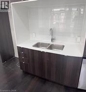 Wood-finish base cabinetry with metal pulls, under-counter double basin stainless steel sink, white countertop, and white subway tile backsplash - 