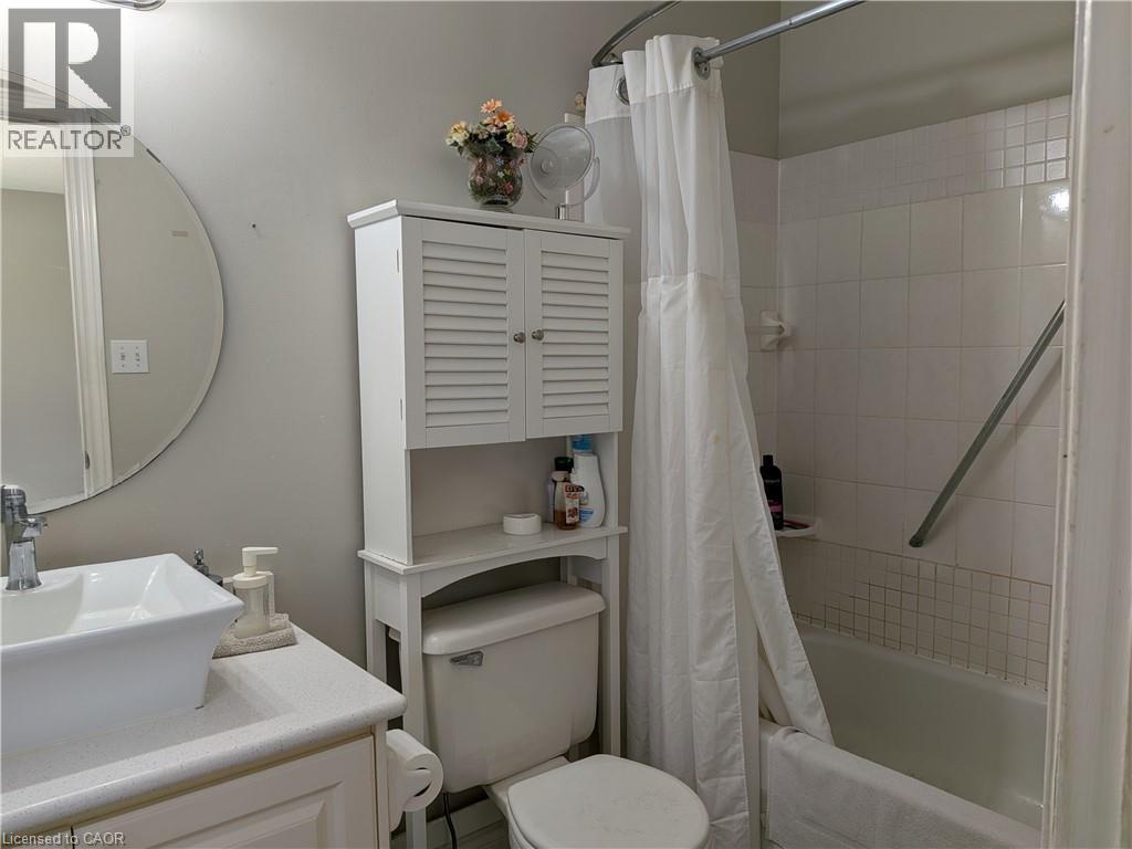 White vessel sink with chrome faucet, white countertop, white built-in storage cabinet, white toilet, and white tiled shower surround with a grab bar - 45 Caswell Drive Unit# Upper, Hamilton, ON - Indoor Photo Showing Bathroom