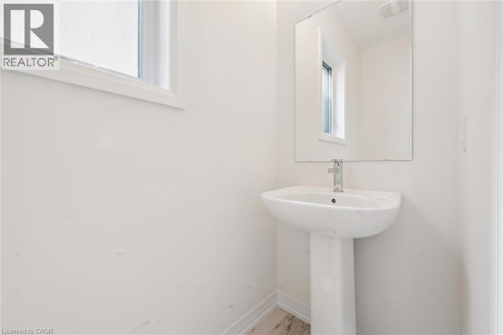 Pedestal sink with chrome faucet, large wall-mounted mirror, and white trim window - 451 Benninger Street, Kitchener, ON